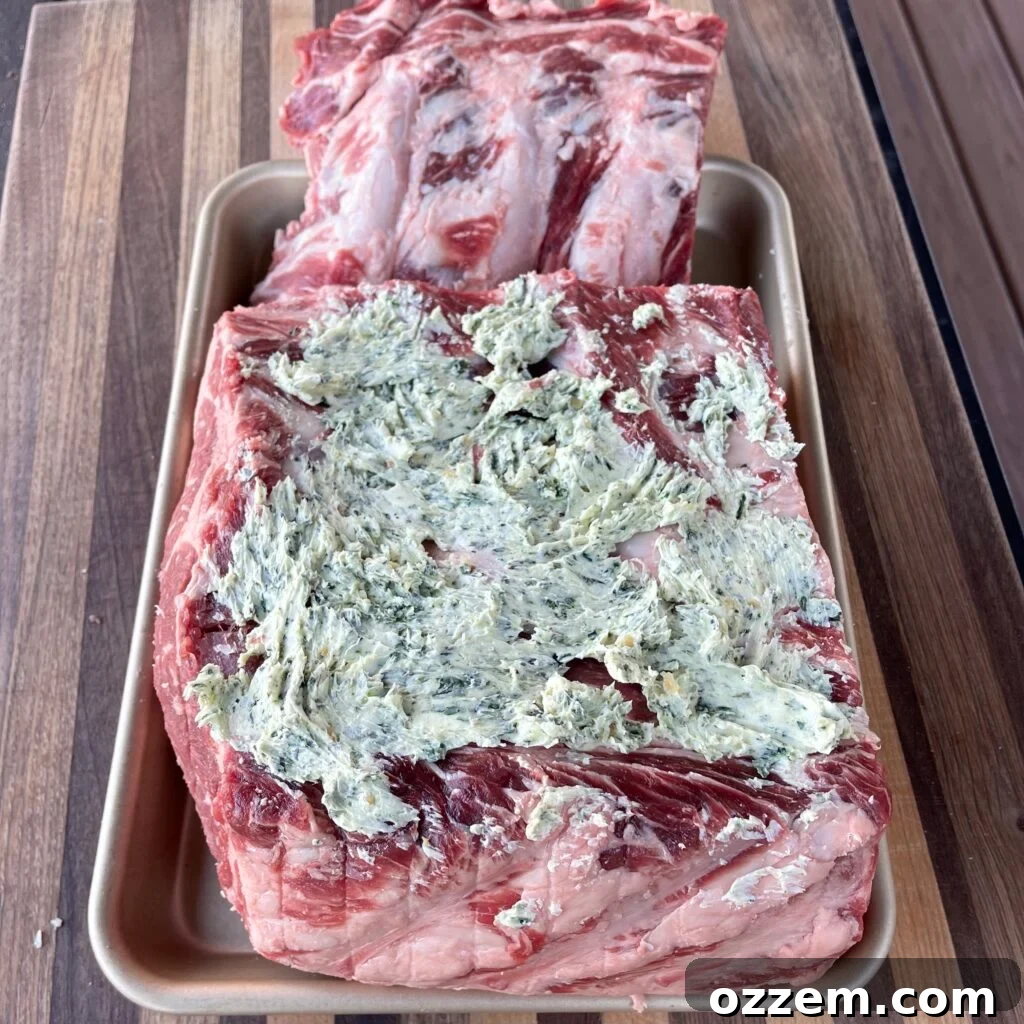 Raw prime rib covered in the garlic and herb compound butter, showing the butter spread between the ribs.