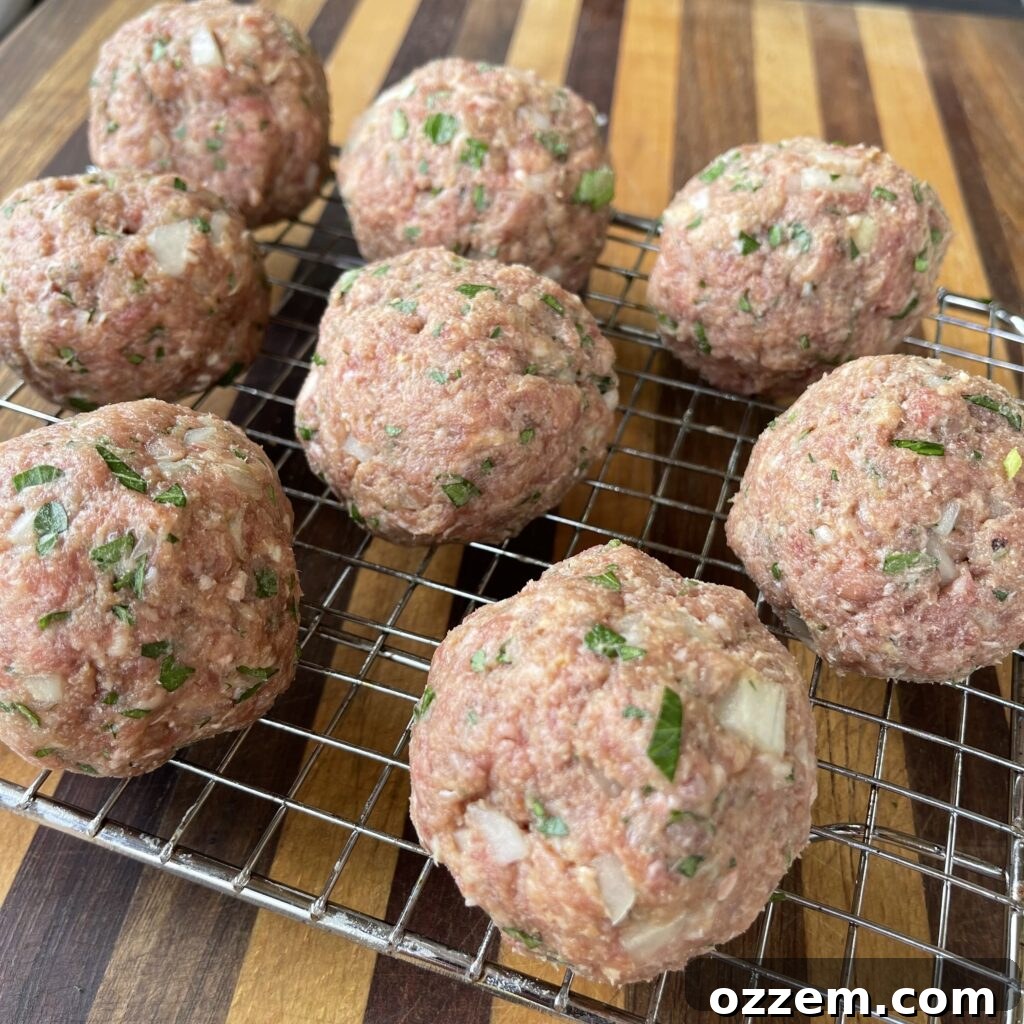Neatly arranged hand-rolled homemade meatballs on a wire rack, prepared for grilling.