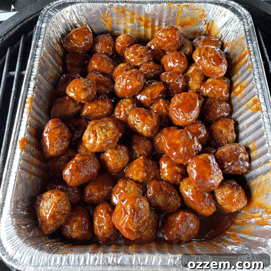 Grilled BBQ cocktail meatballs, beautifully glazed with sauce, resting on the grill for final caramelization.