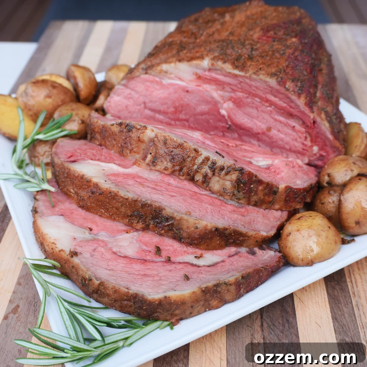 Freshly cooked prime rib that is sliced and served on a white platter with roasted potatoes, ready to be enjoyed.