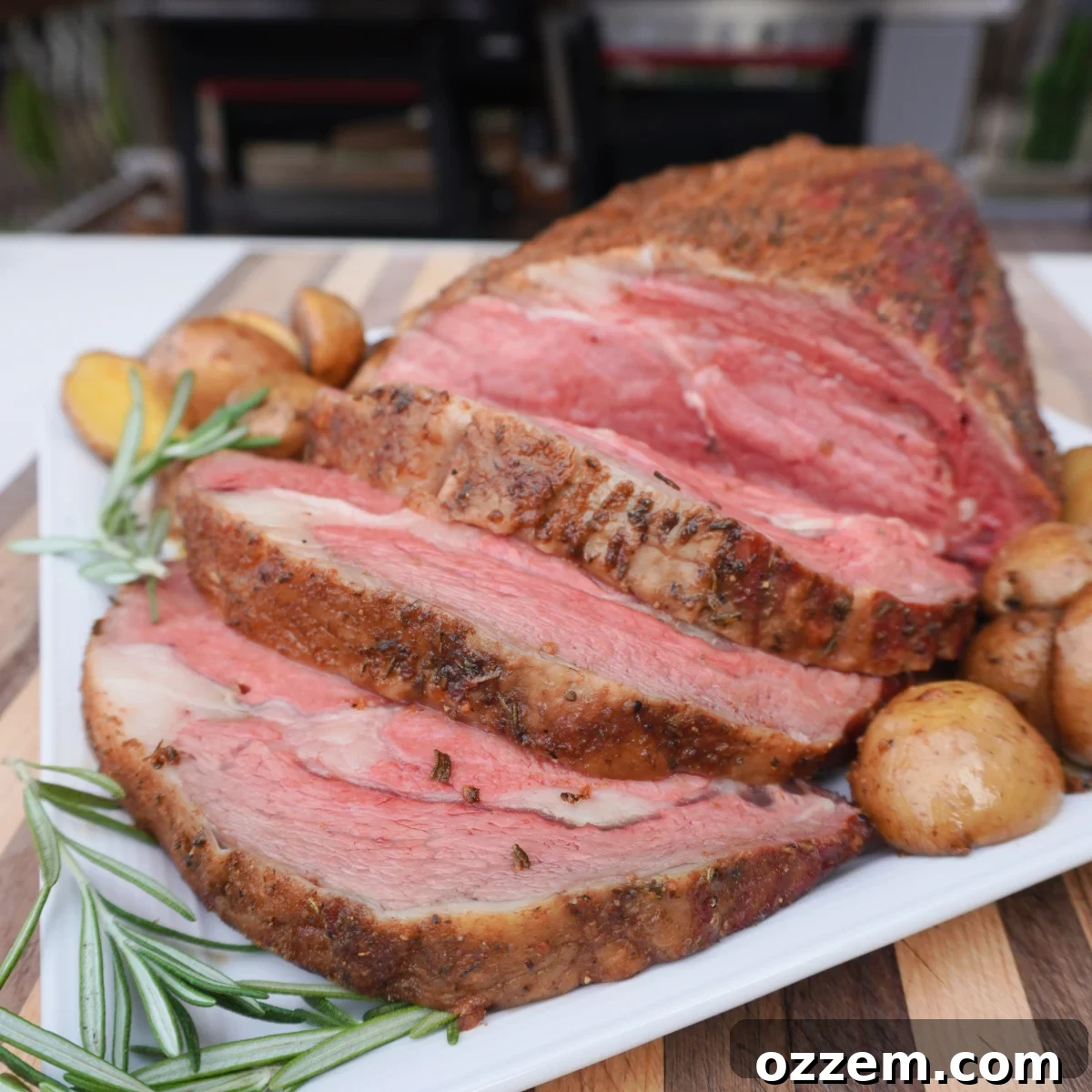 Freshly cooked prime rib that is sliced and served on a white platter with roasted potatoes, complete with horseradish sauce.