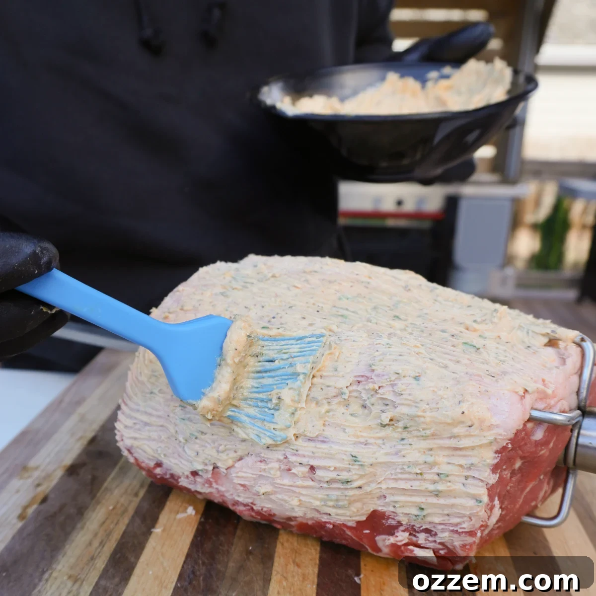Applying the herb compound butter generously to the prime rib before grill placement.