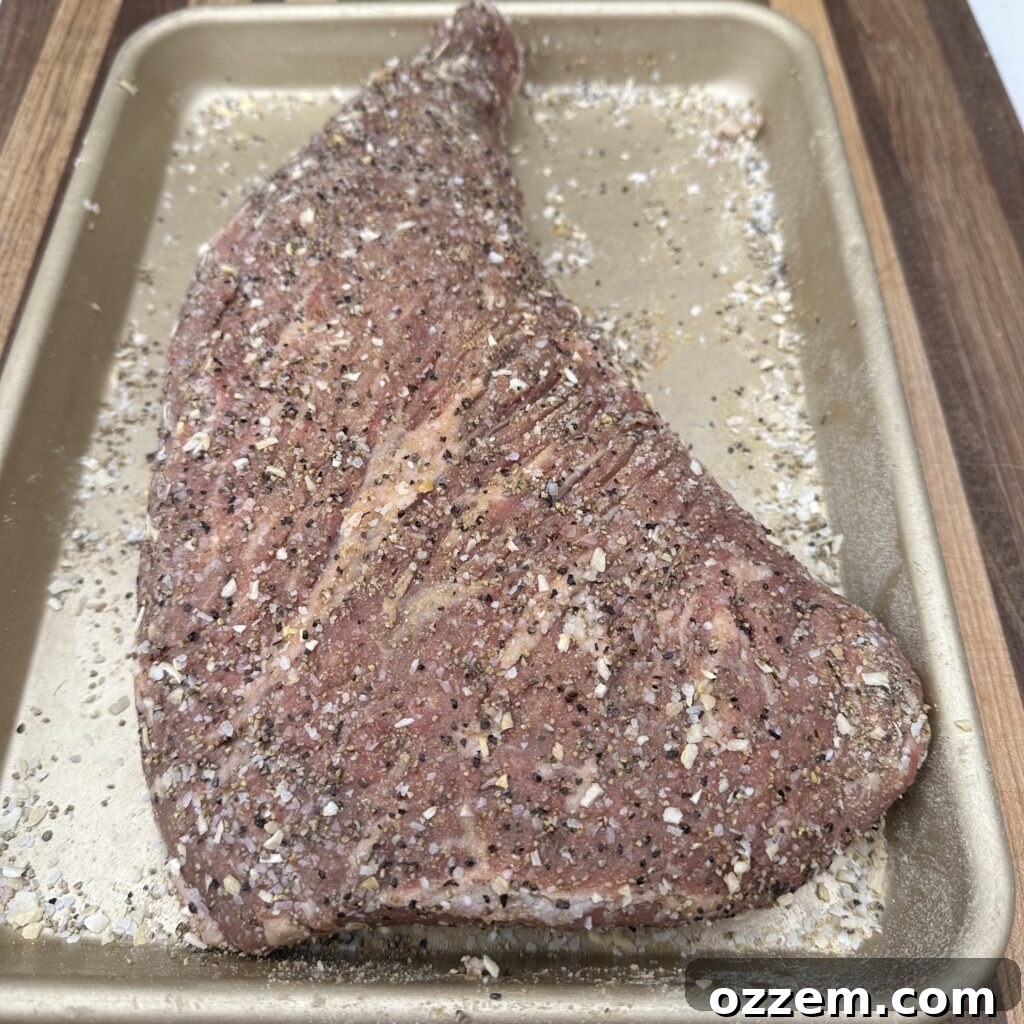 Tri tip steak generously seasoned with salt and pepper, ready for grilling.