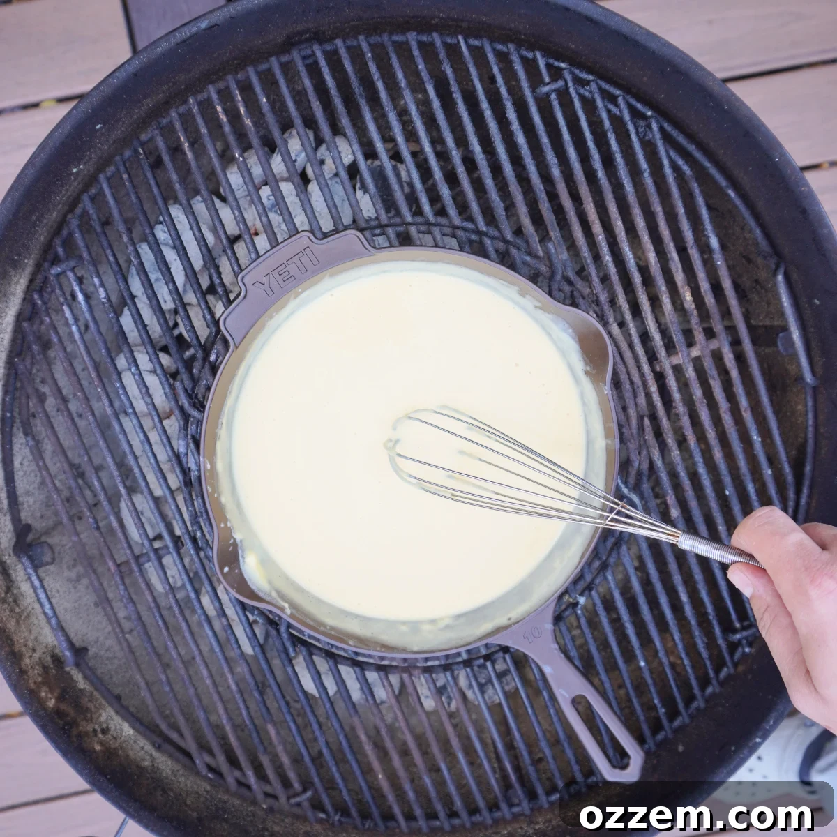Cast iron skillet bubbling with creamy cheese sauce on a grill.