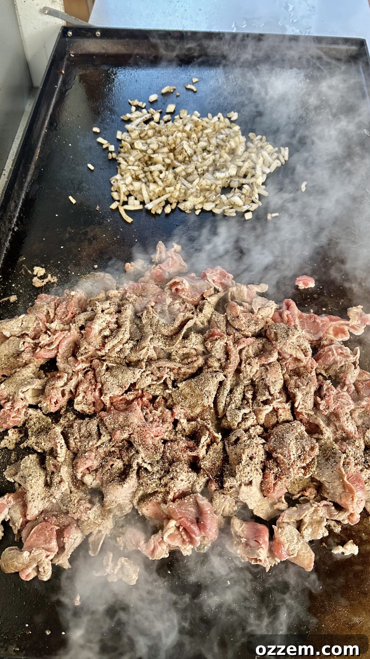 Thinly sliced ribeye steak and cooked onions on a griddle, ready for assembly