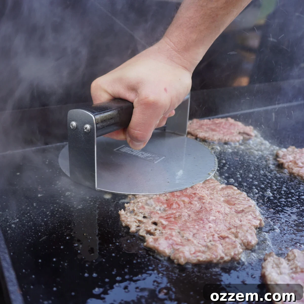 Smashing patties onto a hot griddle with a spatula.