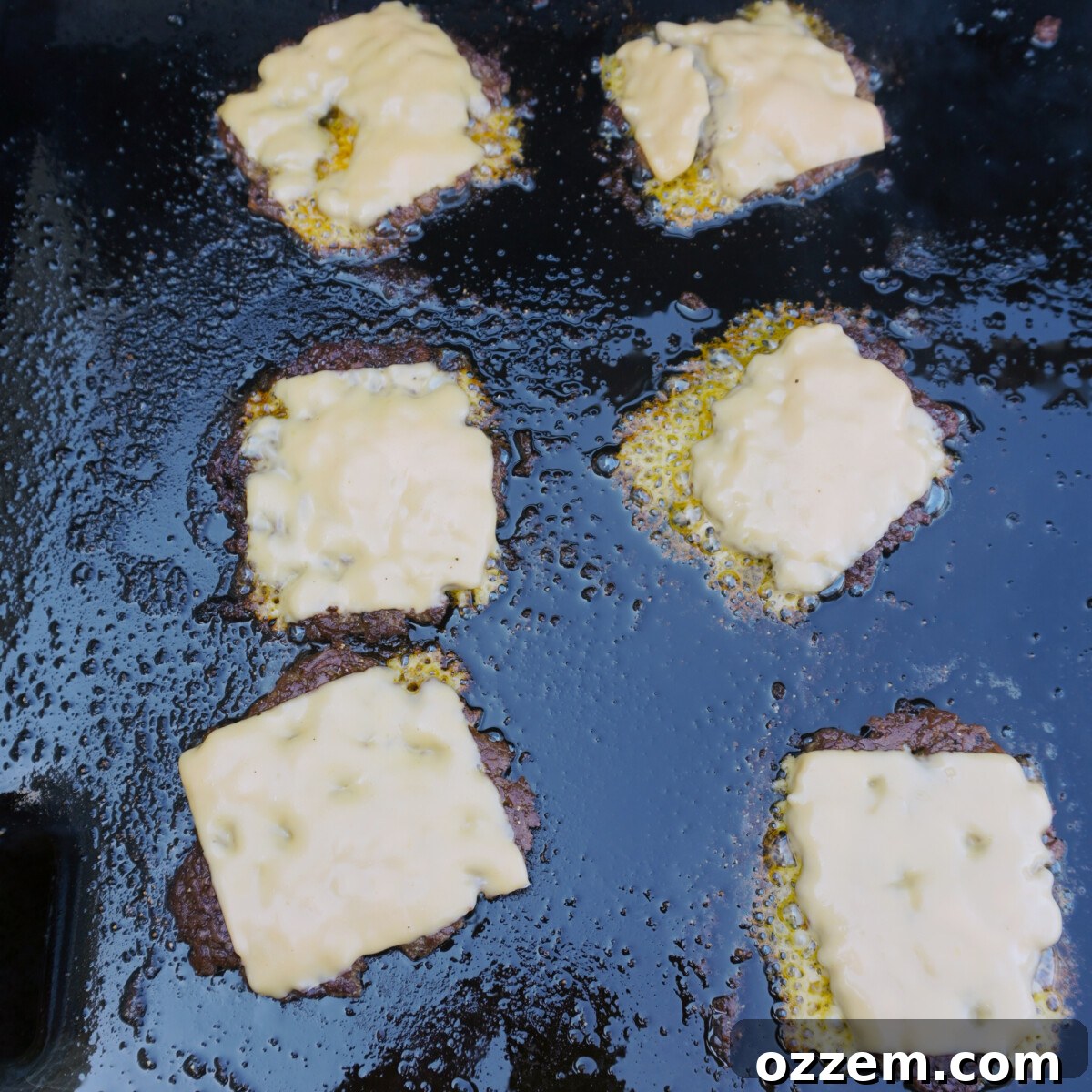 Burger patties on the griddle with melted cheese and sautéed onions.
