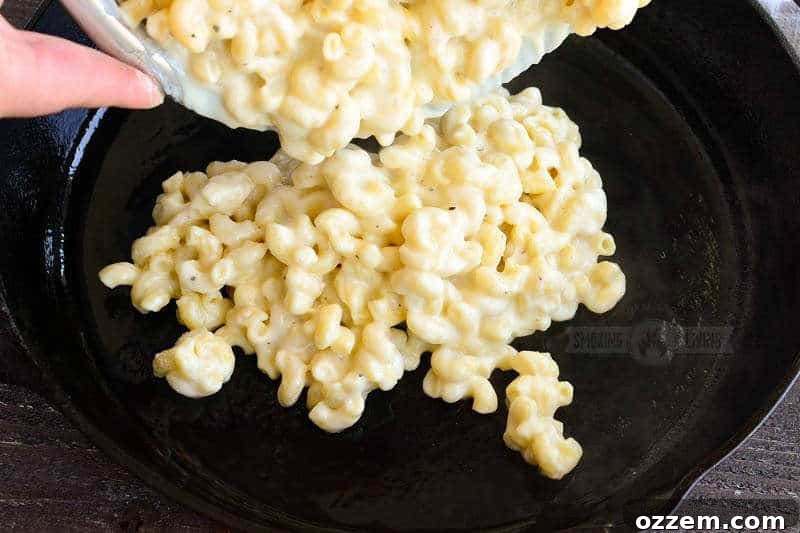 Smoky Mac and Cheese Delight 5 Deliciously cheesy pasta being carefully poured into a greased cast iron skillet, ready for the smoker.
