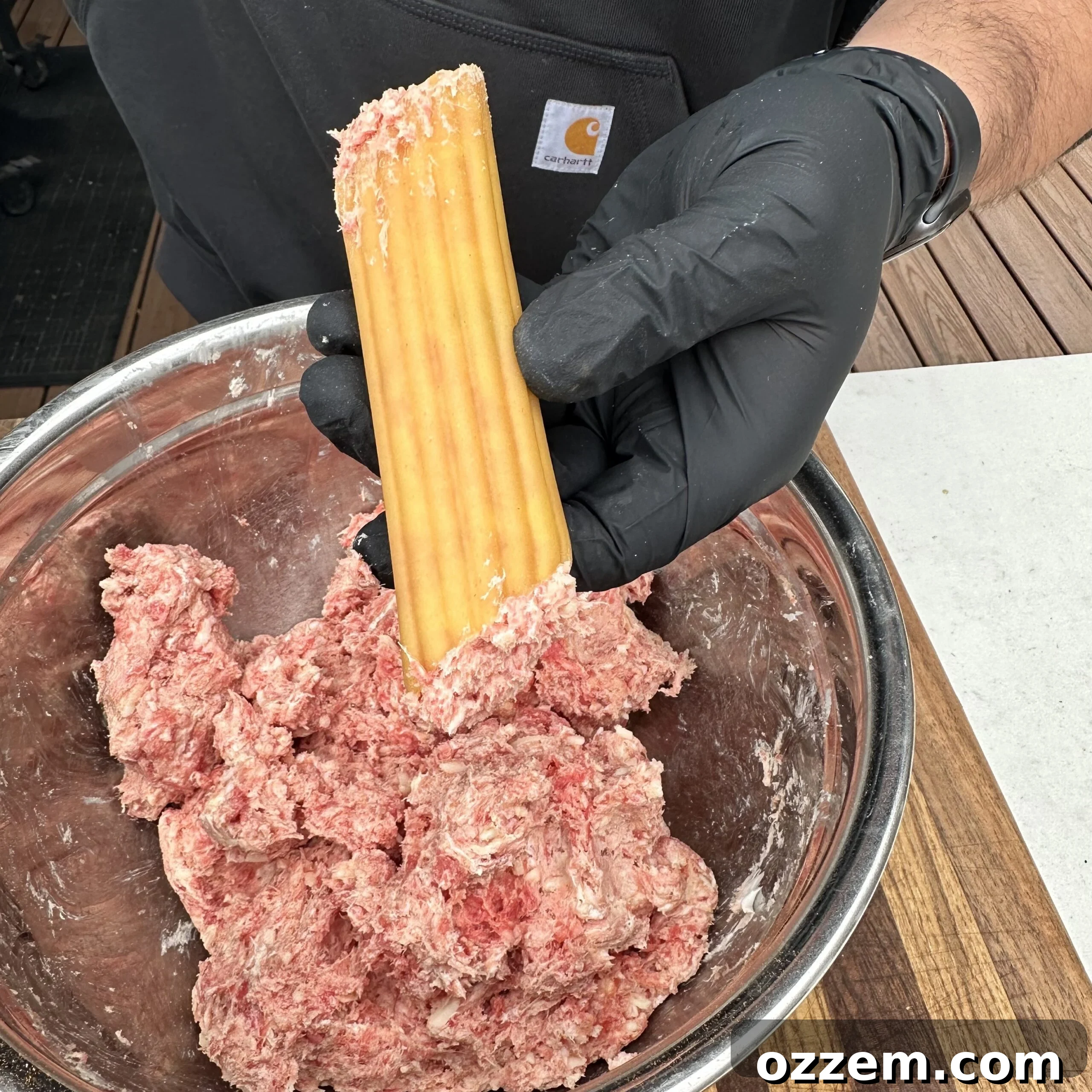 Hands carefully stuffing raw manicotti shells with a savory meat mixture, preparing them for the next step of bacon wrapping.