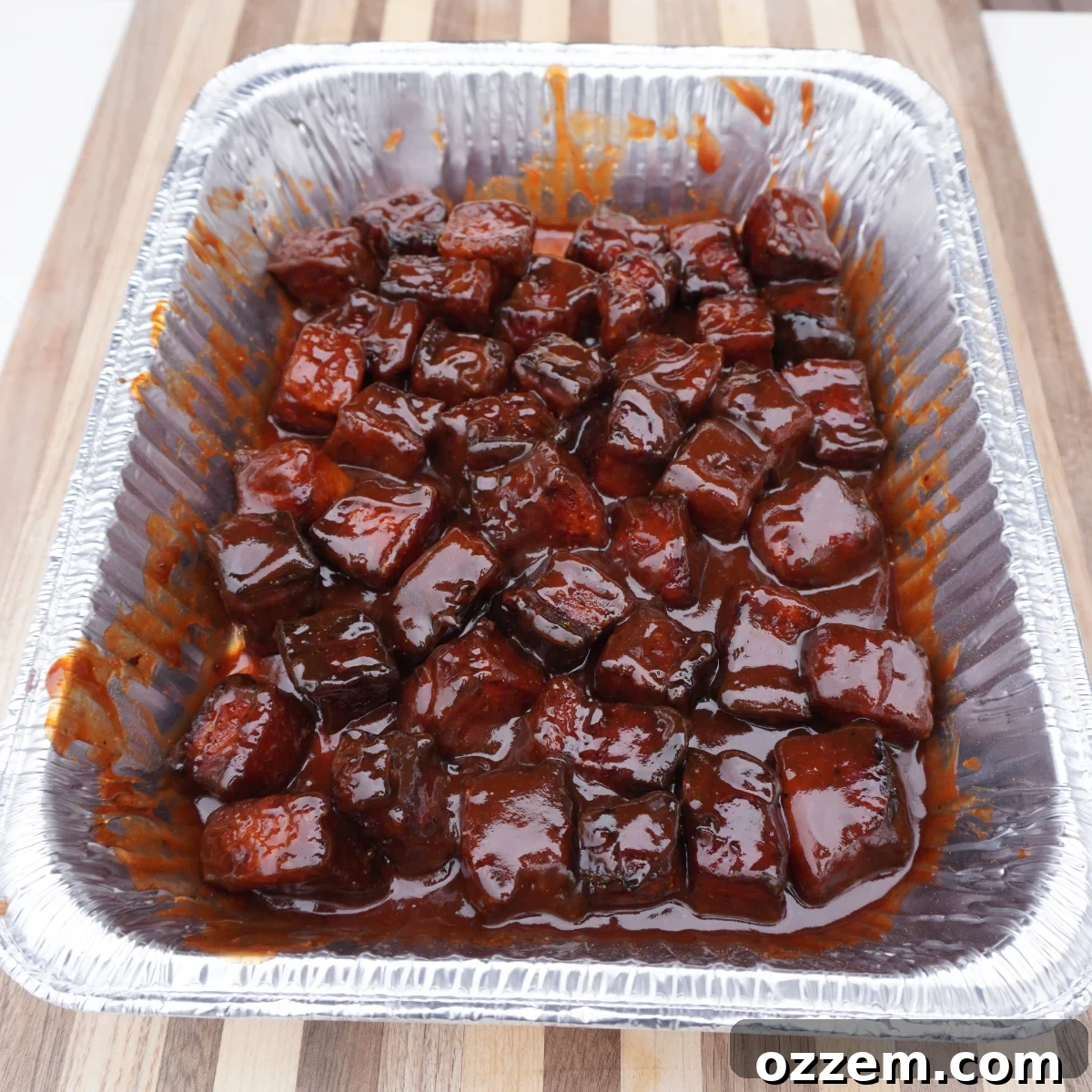 Finished maple bourbon pork belly burnt ends in a foil pan, coated in sauce.