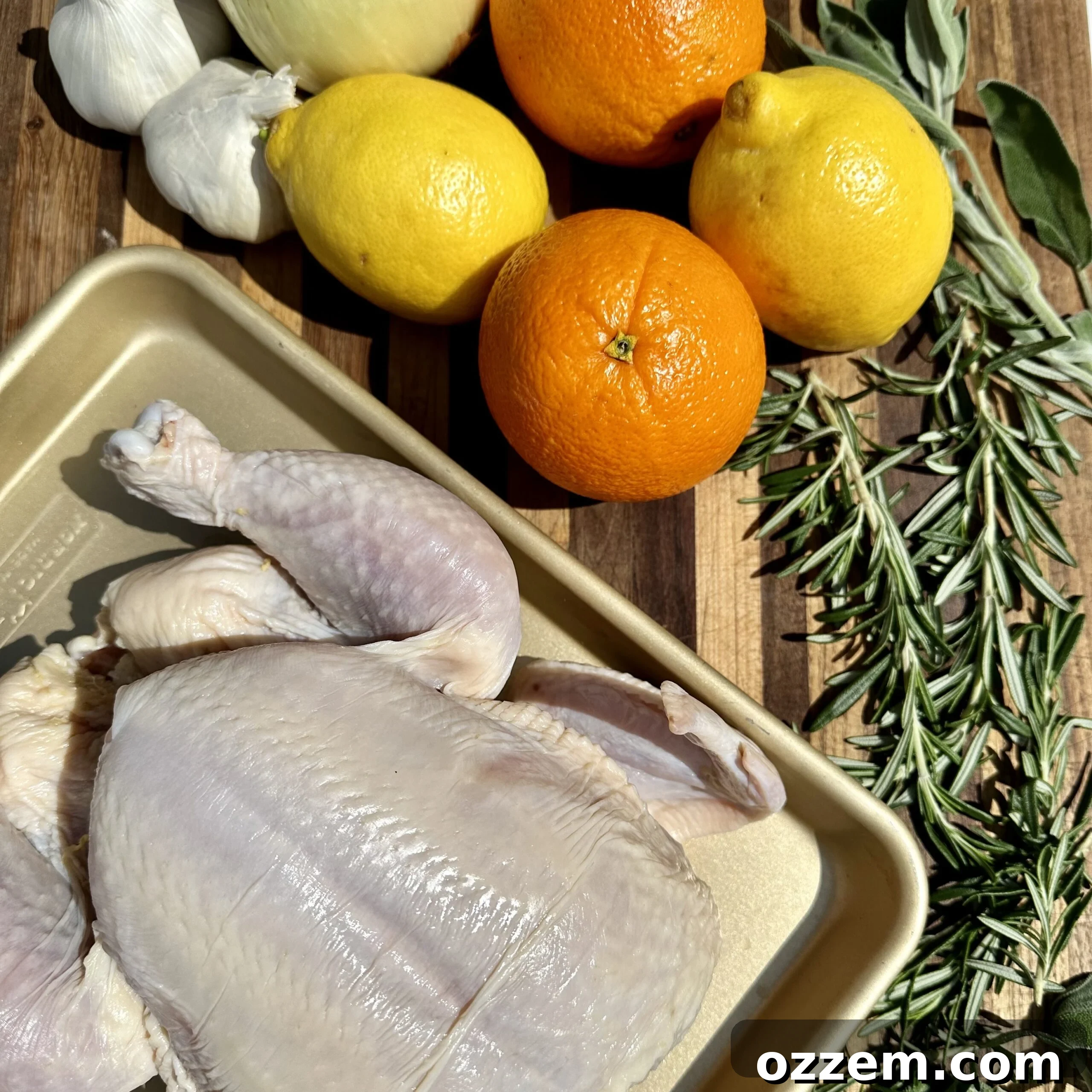 Fresh lemons, oranges, garlic heads, and sprigs of rosemary and sage artfully arranged on a cutting board, ready for the roasted citrus chicken recipe.