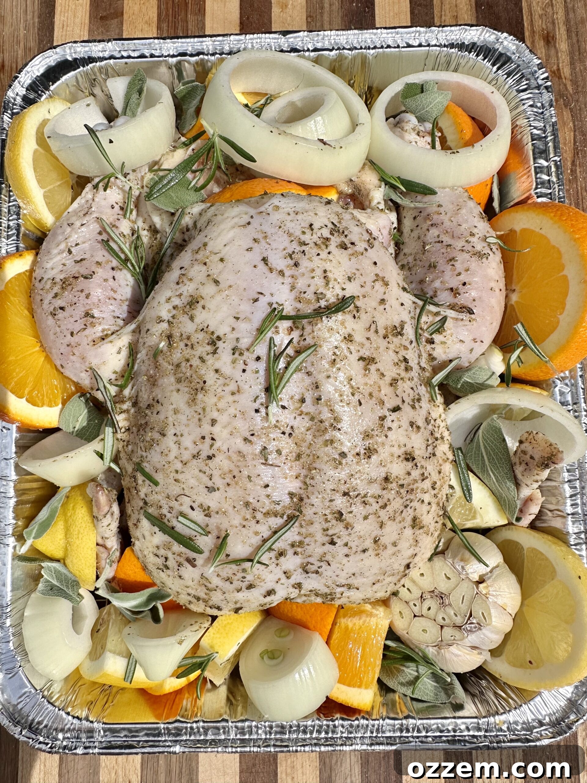 A whole chicken, generously stuffed with citrus fruits and herbs, placed on a wire rack within a roasting pan, ready for cooking.