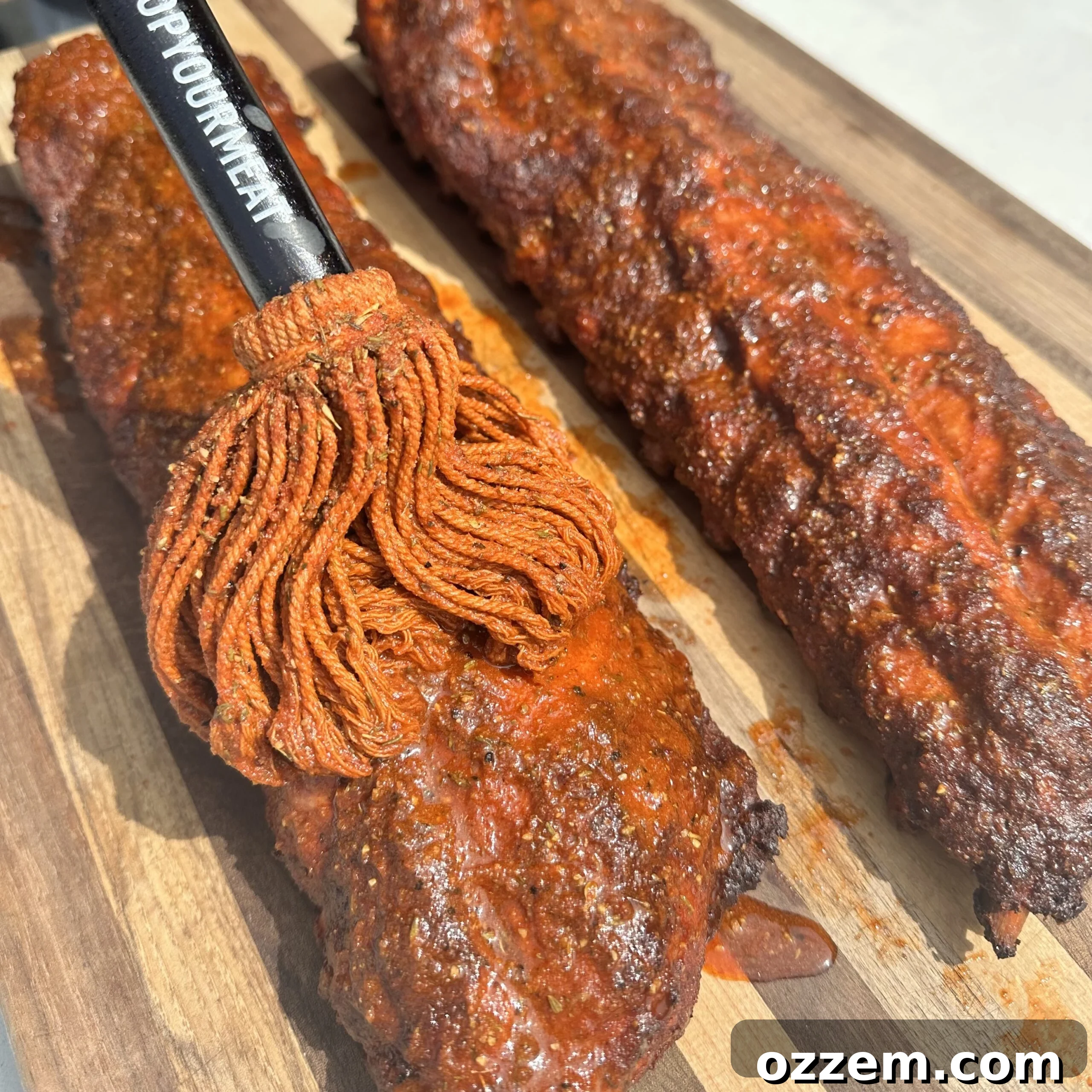 A hand using a basting brush to apply vinegar mop sauce to smoked ribs on a grill grate.