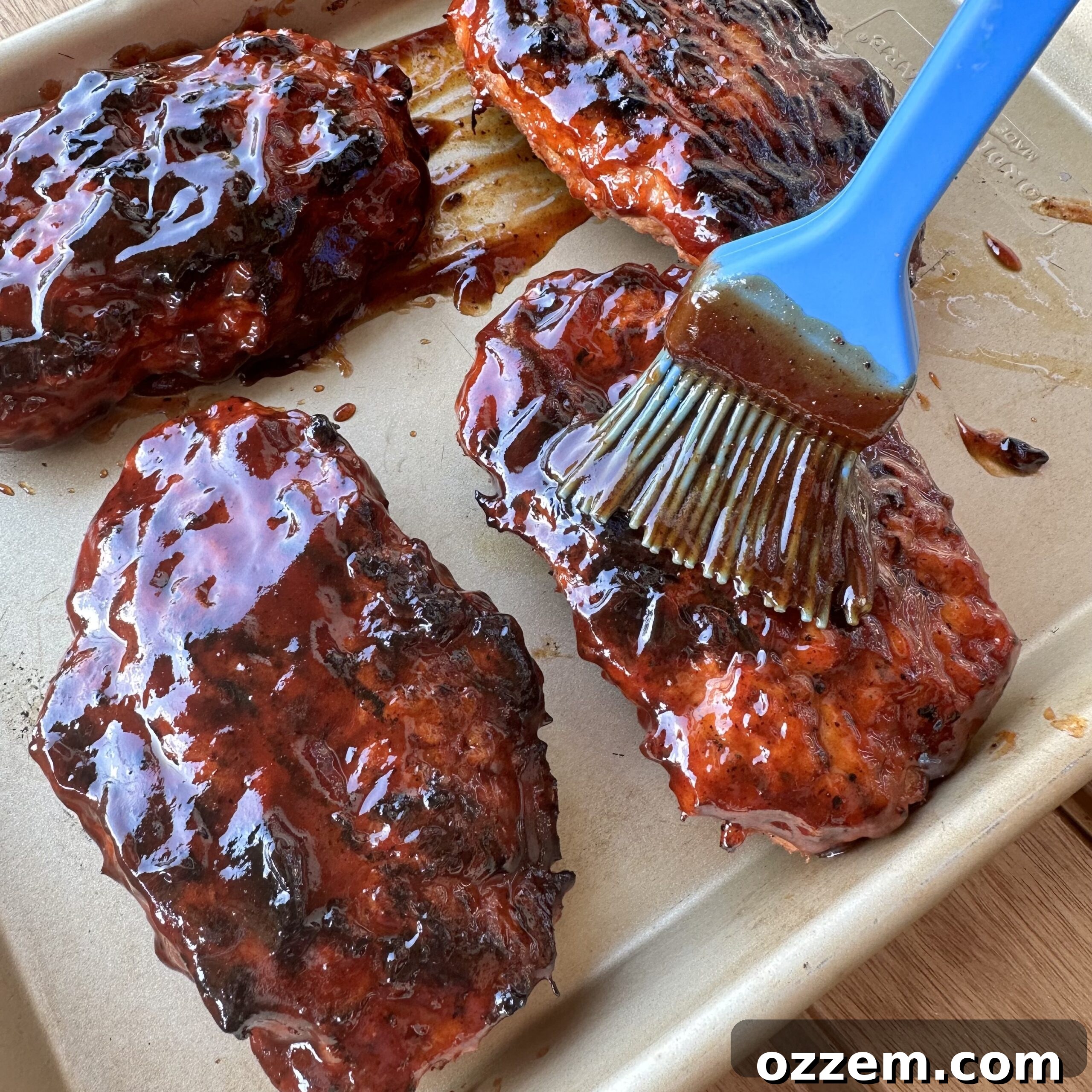 Grilled pork patty being brushed with tangy BBQ sauce