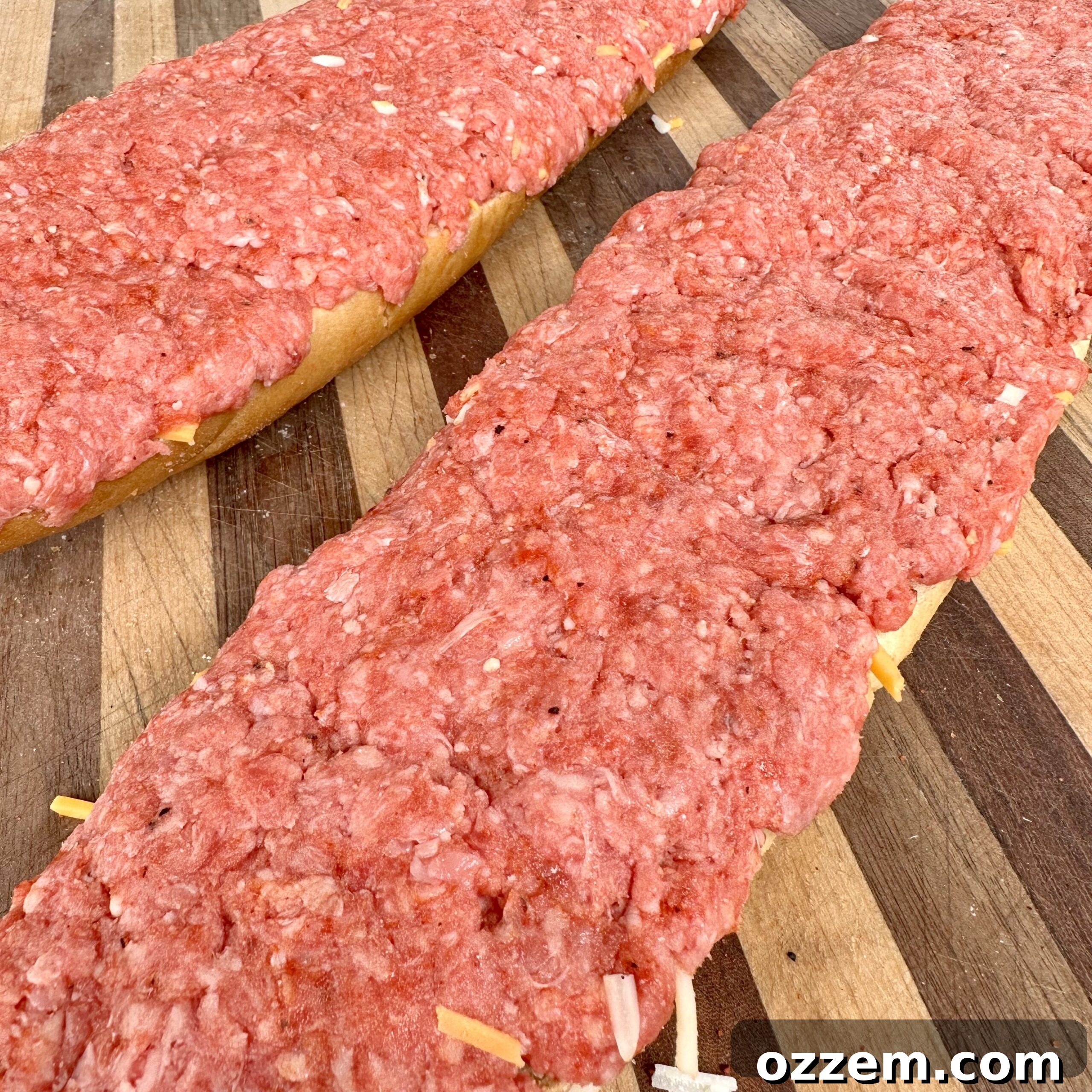 A prepped French bread loaf, carefully hollowed and filled with seasoned ground beef and shredded cheese, ready for grilling
