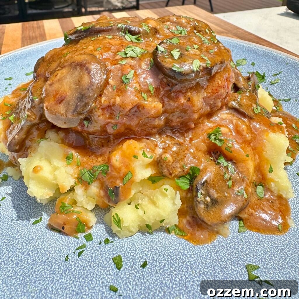 Plated homemade Salisbury steak with rich mushroom gravy and a side of mashed potatoes.