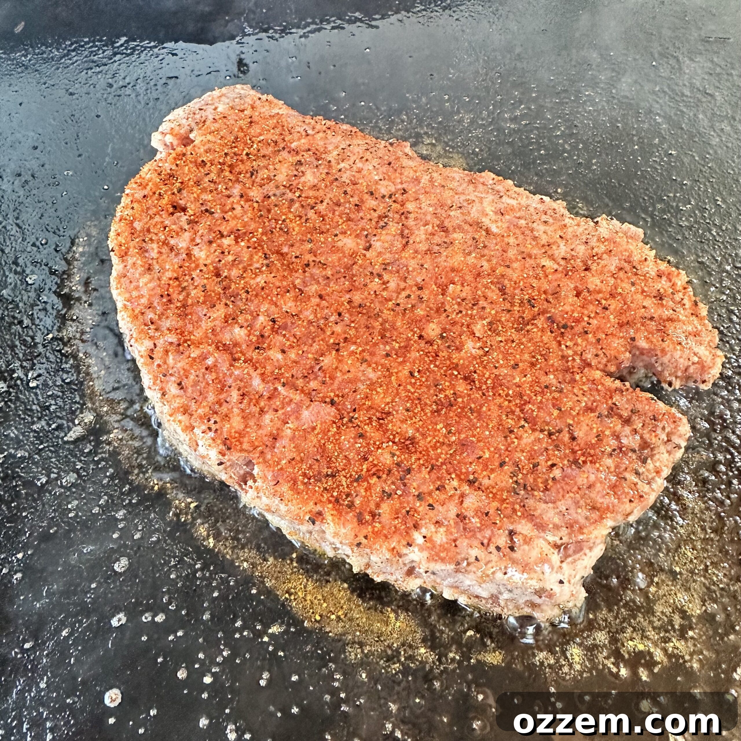 Breakfast sausage patty cooking on a hot griddle, searing to a delicious golden brown.