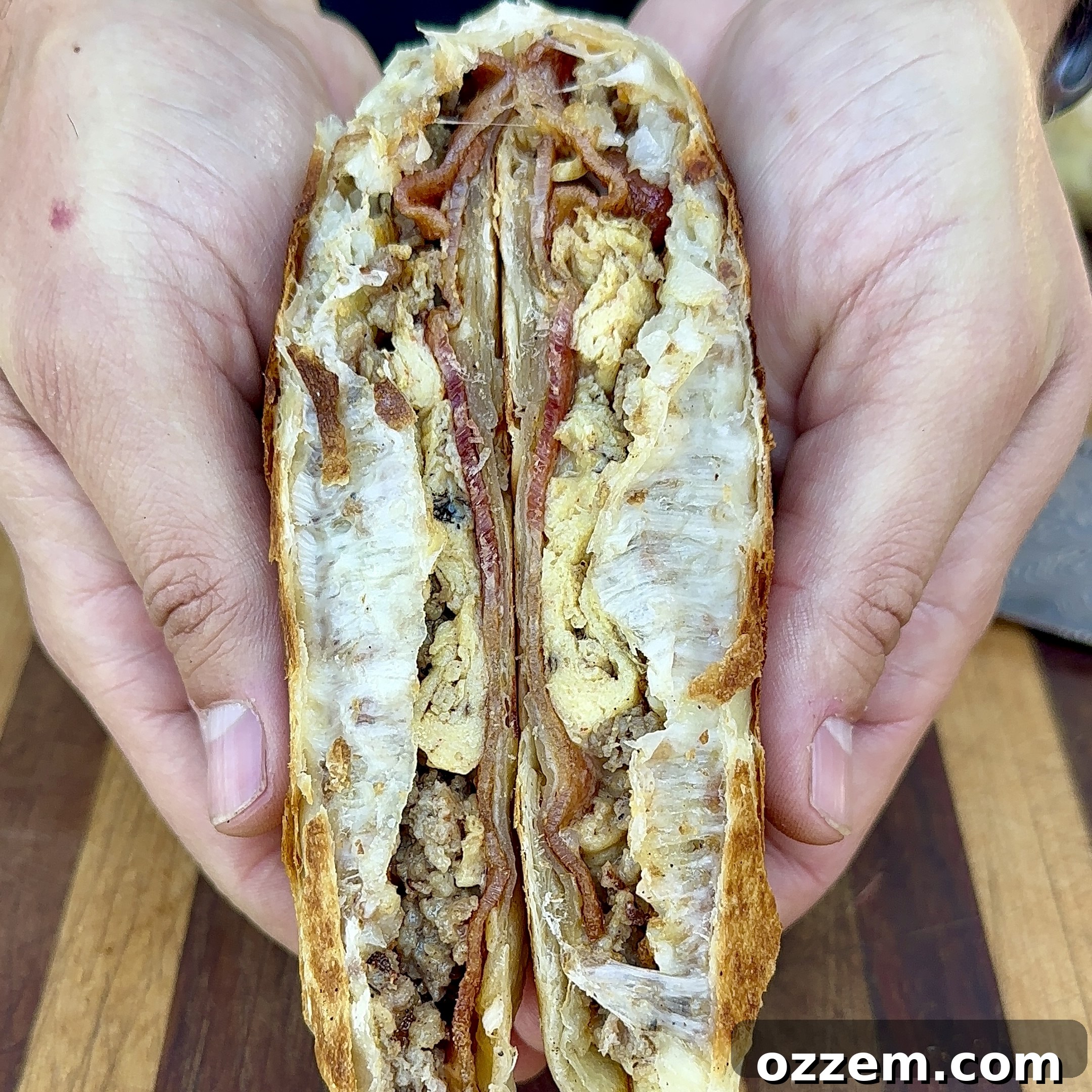 A freshly sliced breakfast crunchwrap revealing layers of eggs, sausage, bacon, hash brown, and cheese.