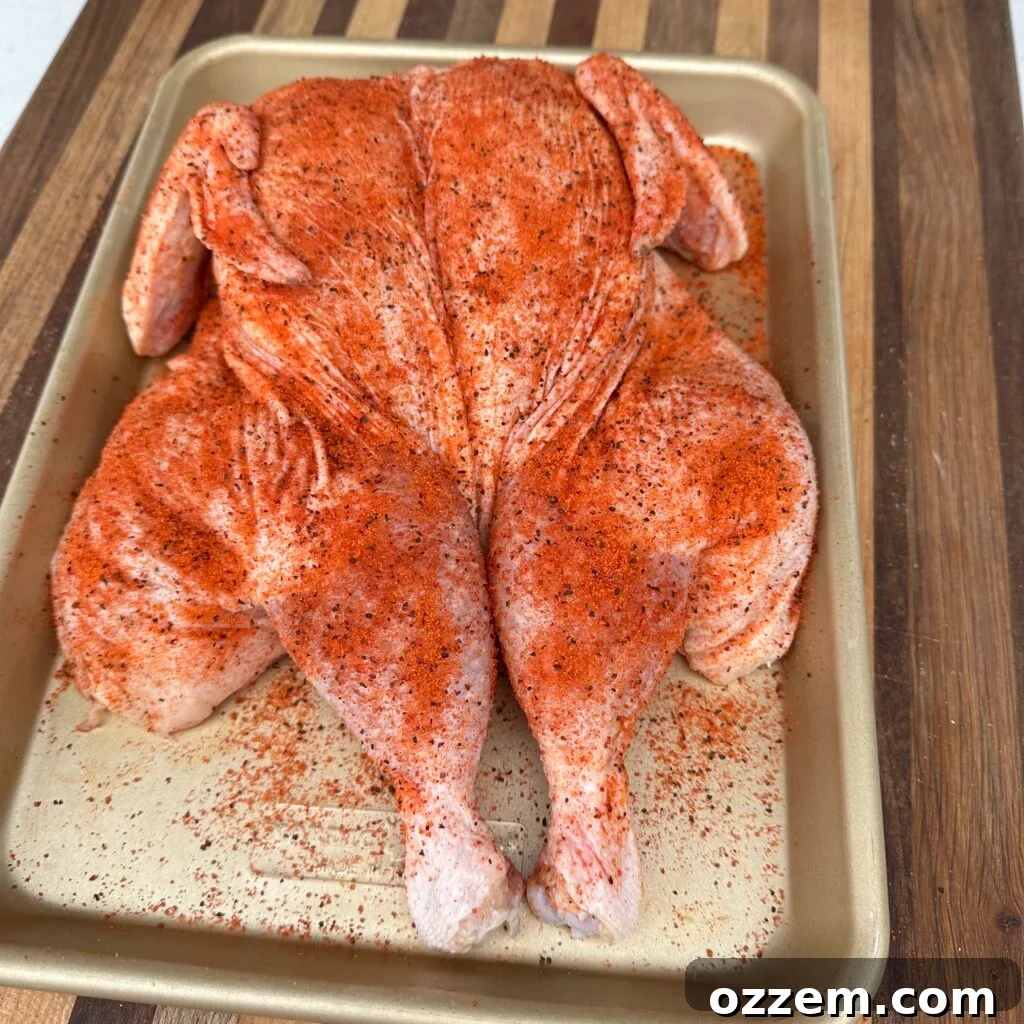 A spatchcocked whole chicken generously seasoned with rub, ready for grilling.