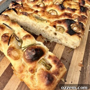 Close-up of a rustic homemade Focaccia bread, glistening with olive oil and topped with fresh herbs.