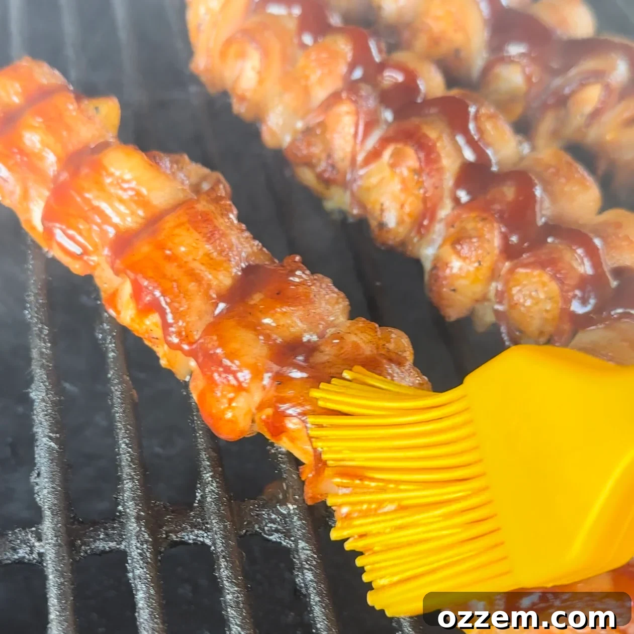 Applying BBQ sauce to grilling chicken skewers with a brush.
