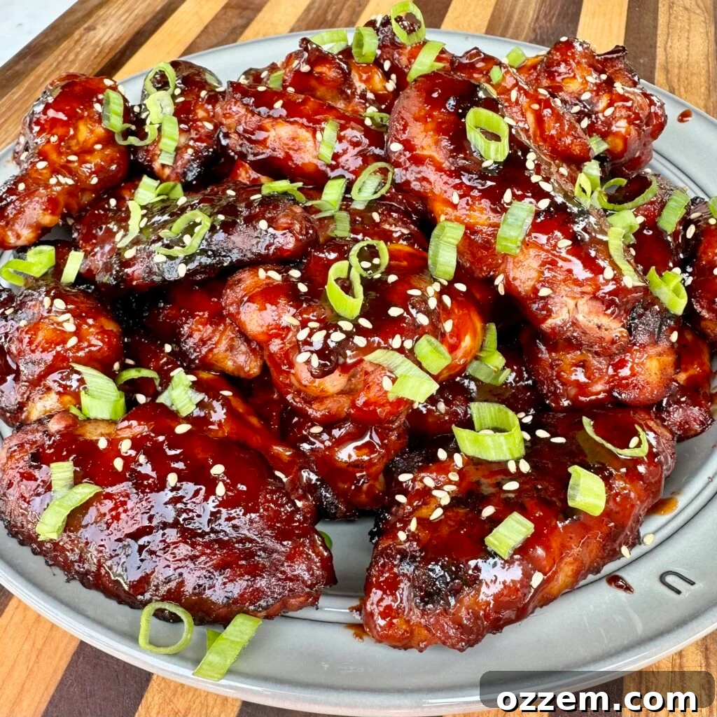 Plated gochujang wings with vibrant red sauce, garnished with toasted sesame seeds and fresh scallions.