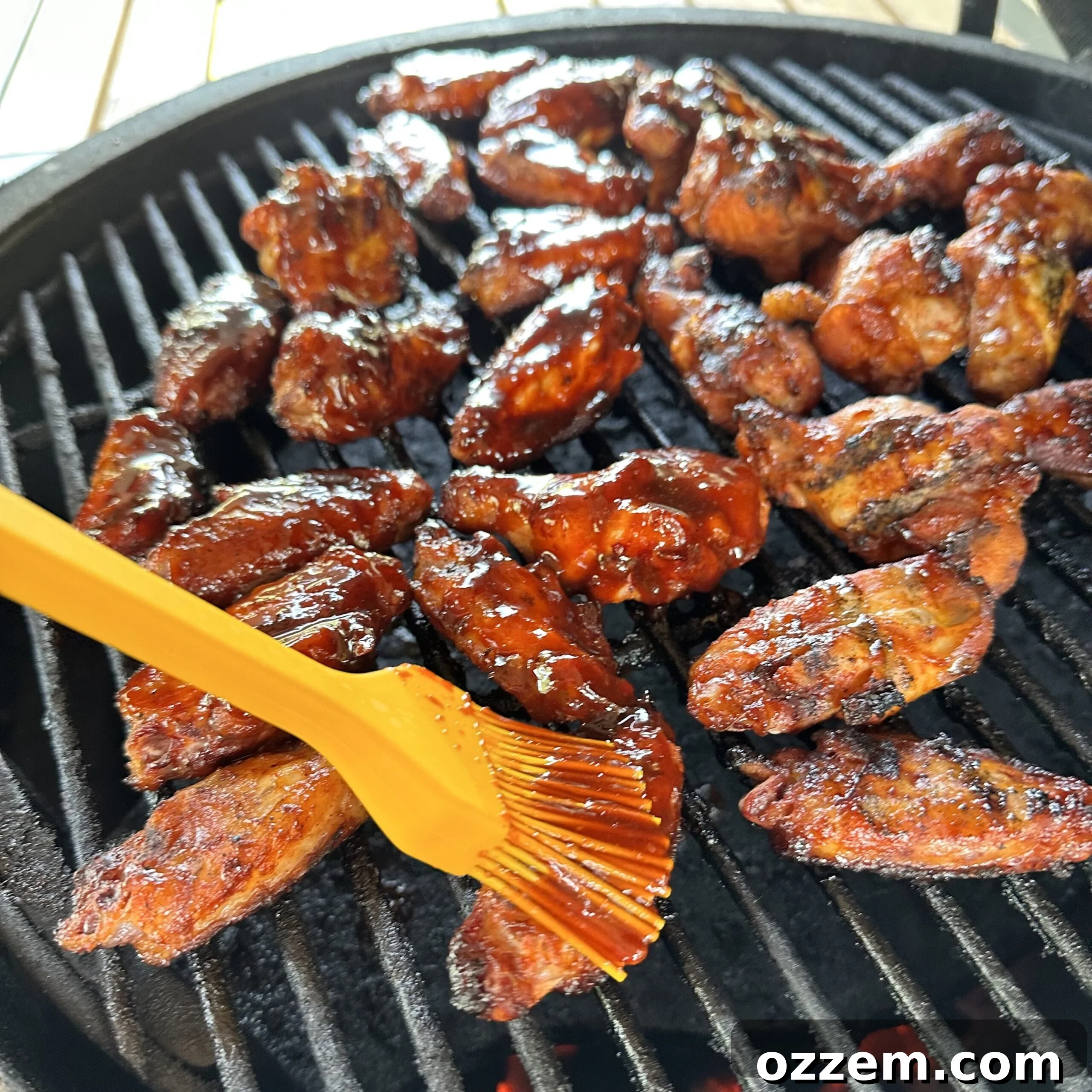 Grilled chicken wings being brushed with gochujang sauce for the final glaze, showing a sticky, vibrant coating.