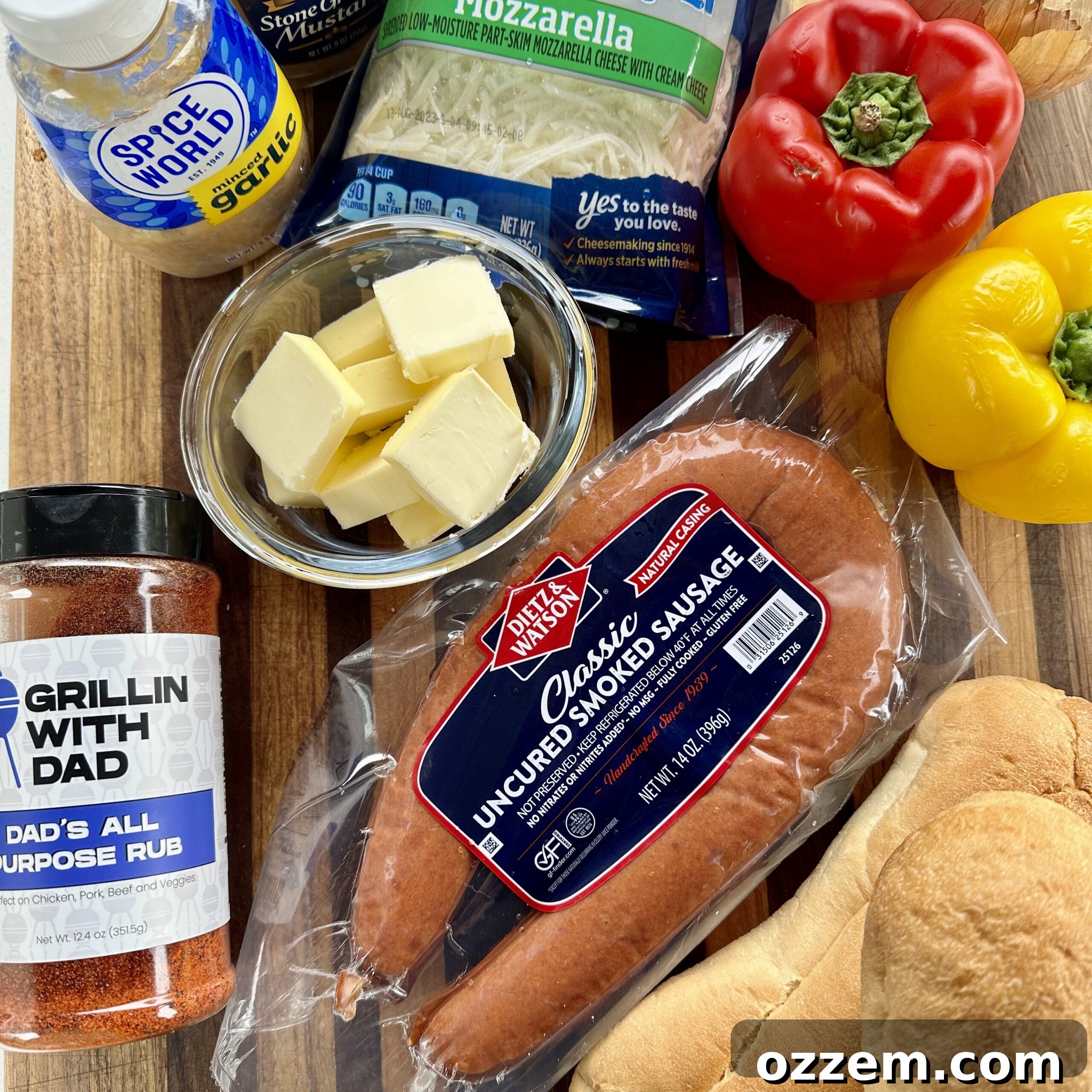Sausage Sub ingredients including sausages, bell peppers, onion, cheese, and rolls laid out on a cutting board.