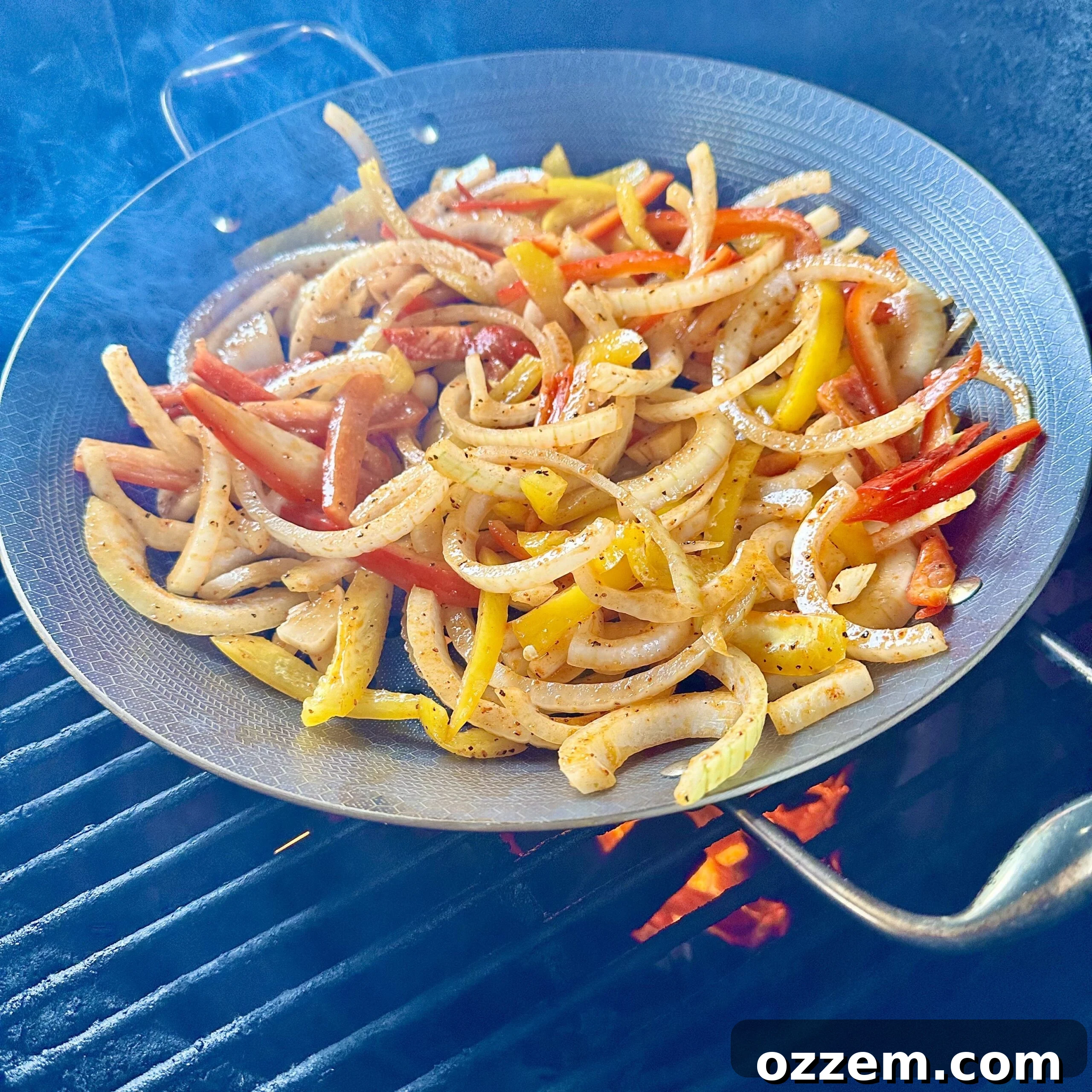 Colorful bell peppers and sliced yellow onions sautéing in a wok on a hot grill, emitting steam.