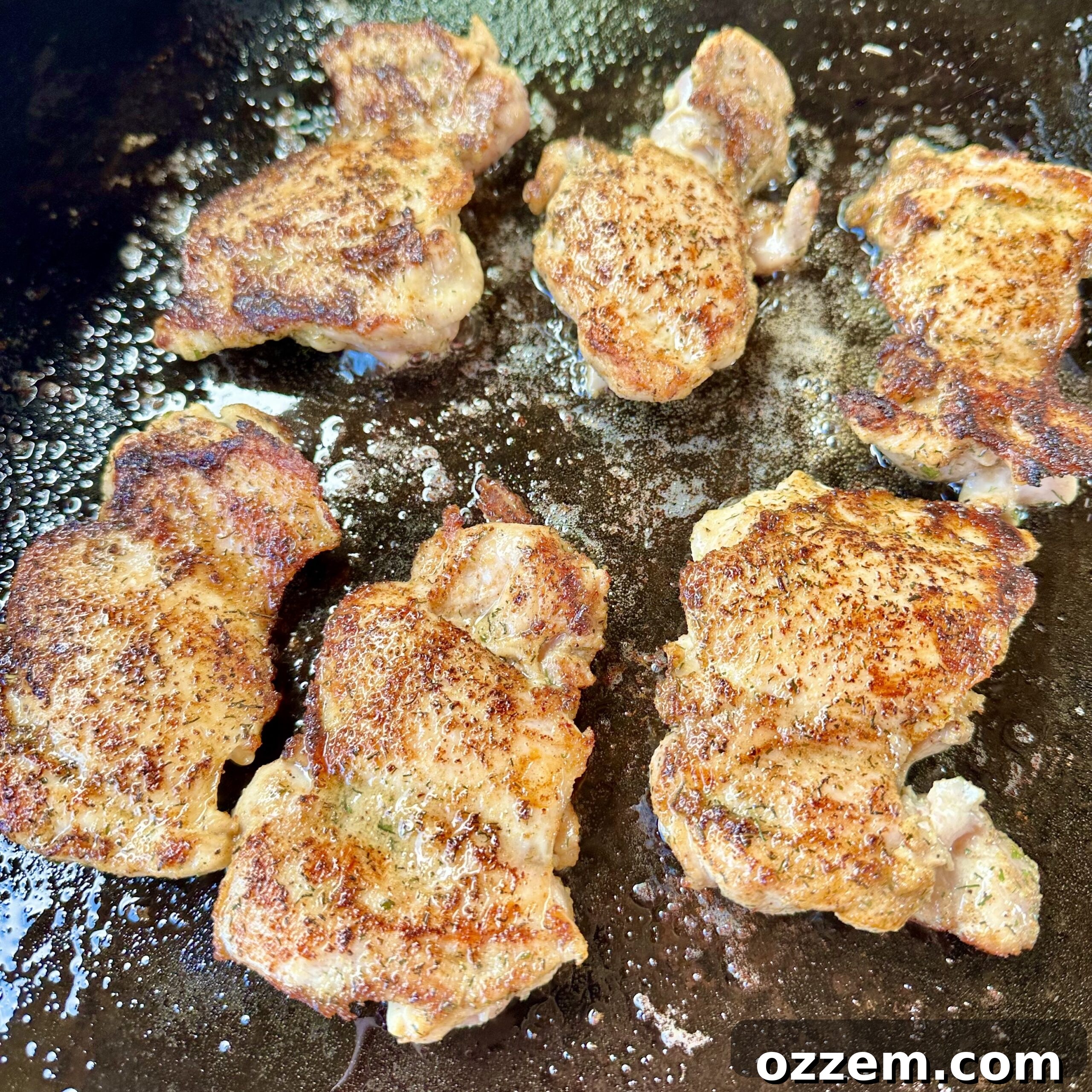 Chicken thighs sizzling on a hot griddle with bacon grease