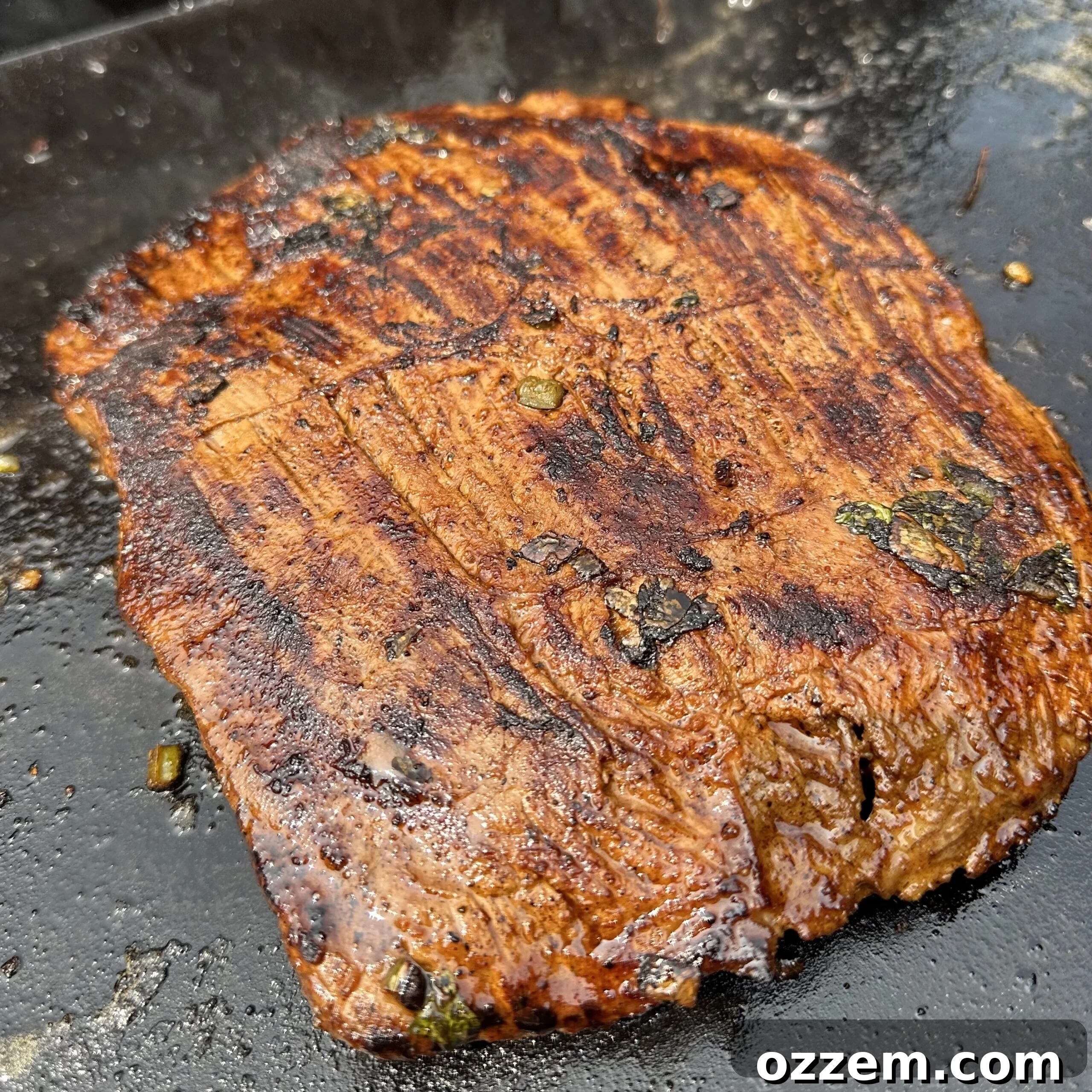 Grilled flank steak sizzling on a flat top griddle