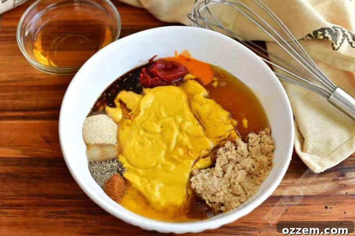 Ingredients for Carolina mustard sauce in a bowl on a wood surface and a whisk beside it.