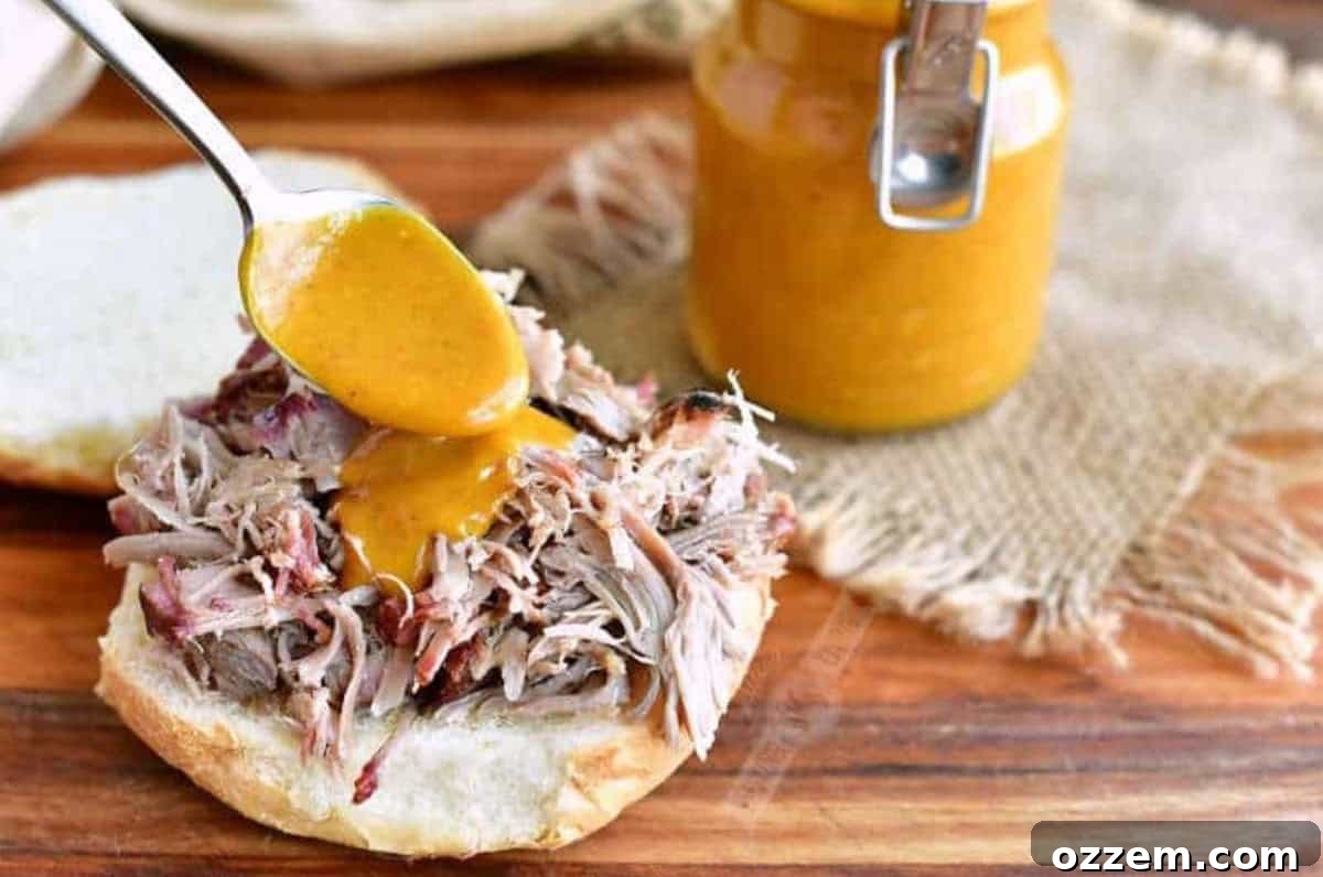 Pouring Carolina mustard sauce with a spoon over pulled pork that is on a bun.