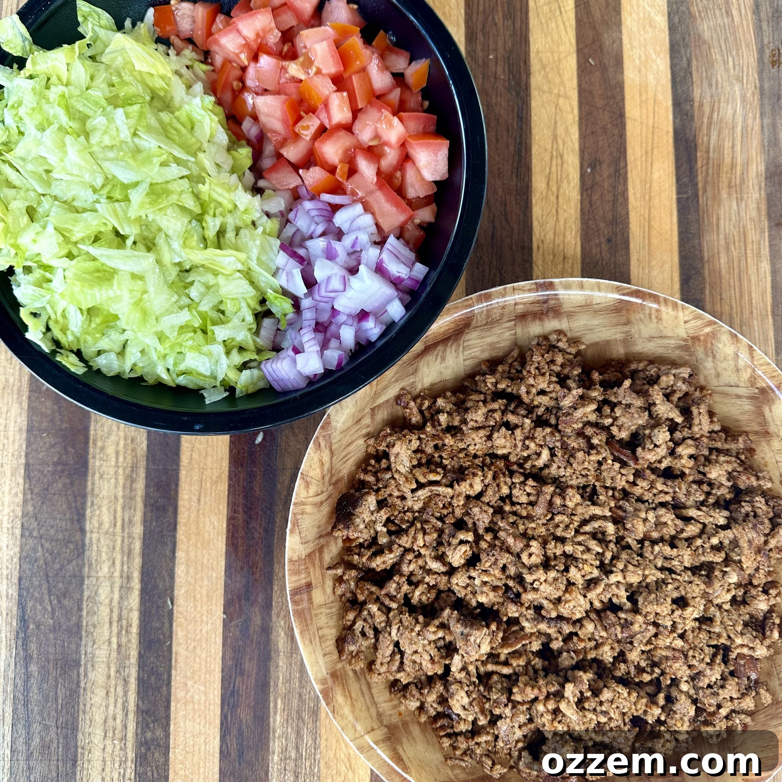 Various ingredients for taco dip, including cooked ground beef, fresh vegetables, and cheese, prepped and ready for assembly.