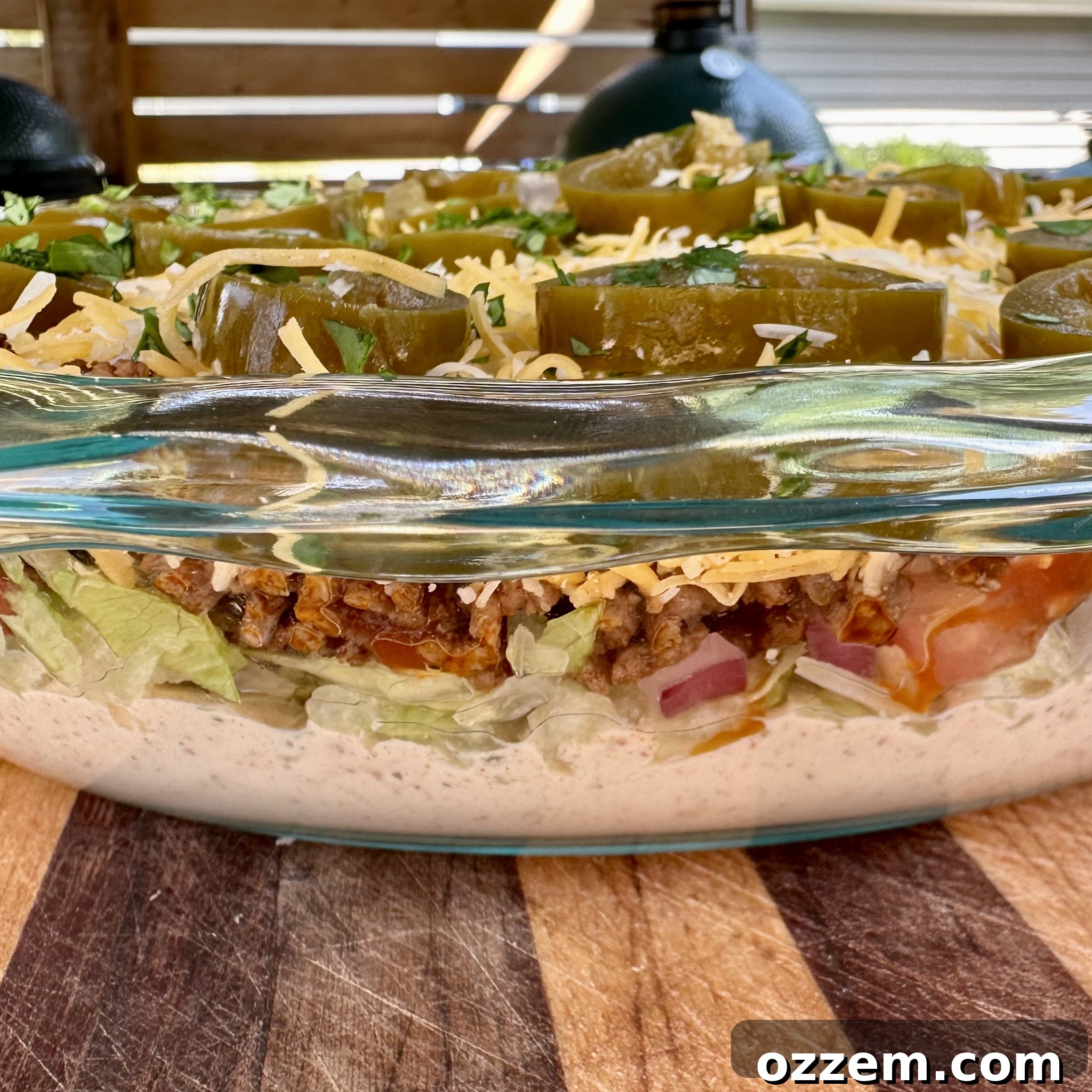 Close-up of a beautifully layered taco dip with visible layers of meat, vegetables, cheese, and creamy sauce.
