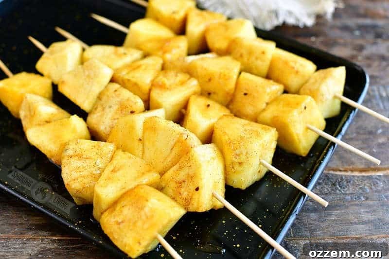 pineapple pieces coated in sugar mixture on skewers on a black metal sheet
