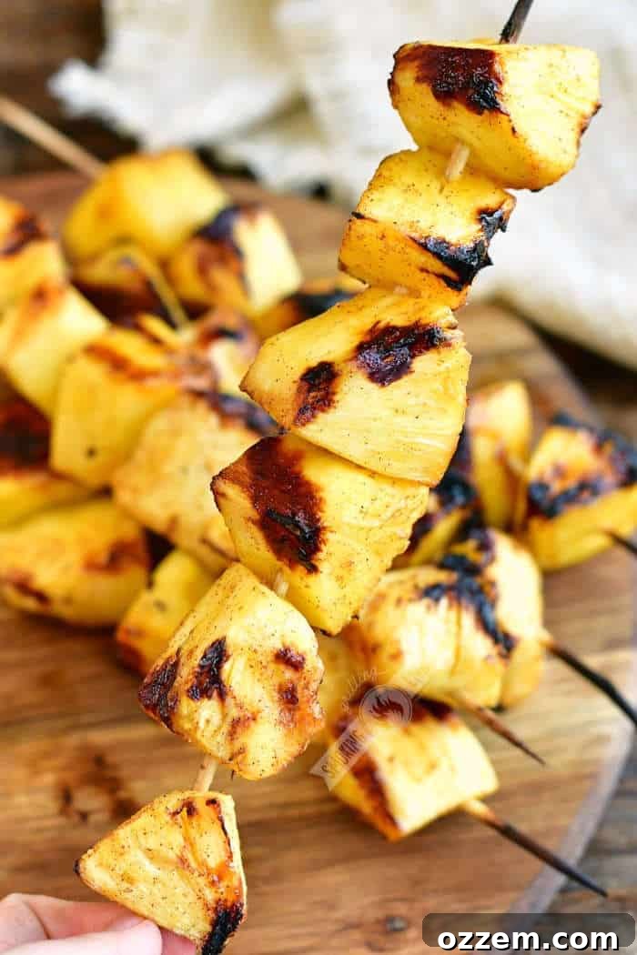 holding a skewer of grilled pineapple chunks