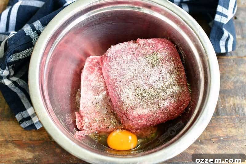 A mixing bowl filled with ground beef, seasoned with salt and pepper, and an egg ready to be incorporated for burger patties.
