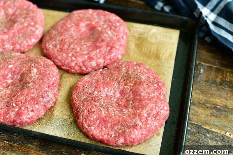 Raw burger patties on a baking sheet, each with a small indentation in the center to prevent bulging during cooking.