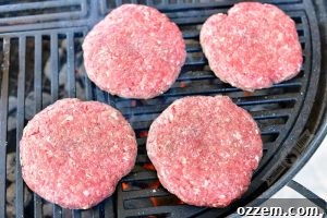 Four uncooked burger patties, each with a dimple, placed directly on the hot grill grates, ready to sear.