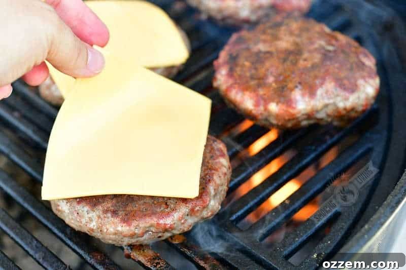 A slice of American cheese being carefully placed on a perfectly cooked burger patty on the grill, melting gently.