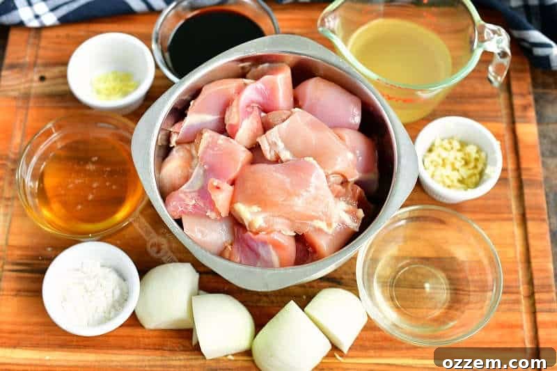 Bowls of teriyaki chicken kebab ingredients on a wooden cutting board: cut chicken, chopped onions, corn starch, minced garlic, rice vinegar, honey, chicken broth, soy sauce, and fresh ginger.