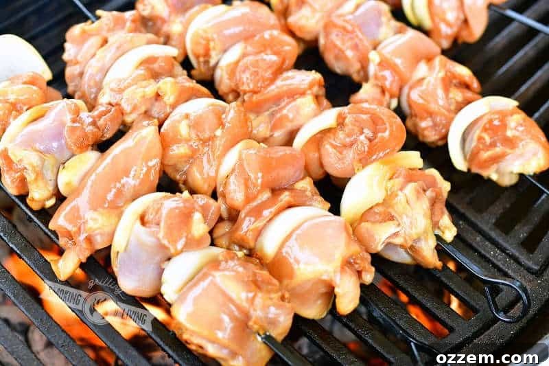 Uncooked teriyaki chicken and onion skewers arranged on a grill over hot coals, ready for cooking.