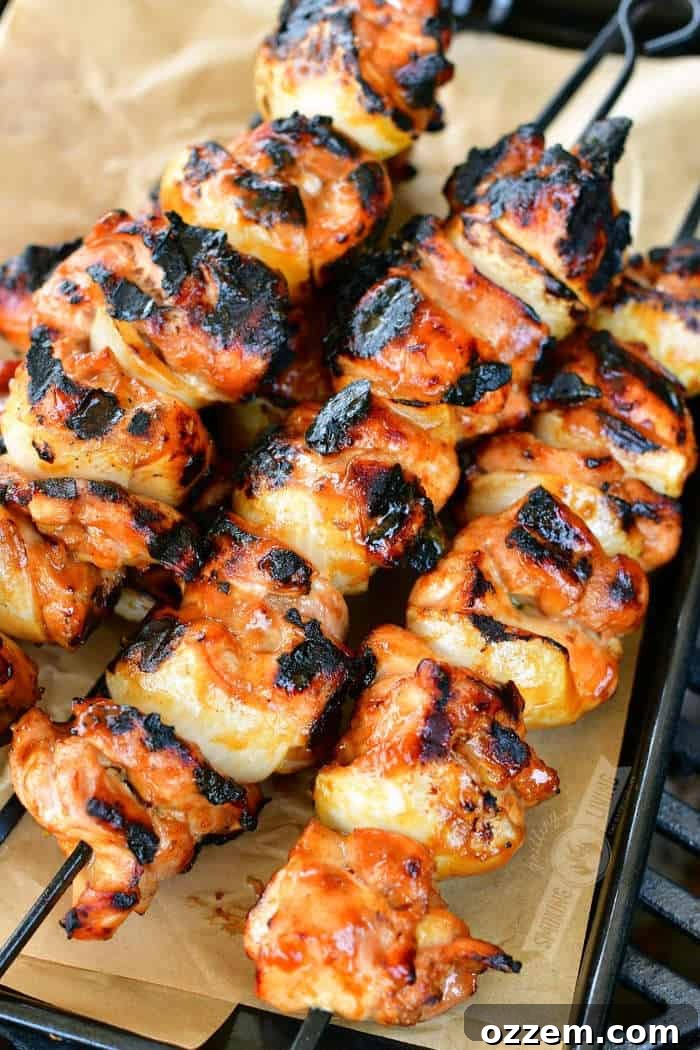 Two black skewers filled with perfectly grilled teriyaki chicken pieces, resting on a black tray lined with parchment paper.