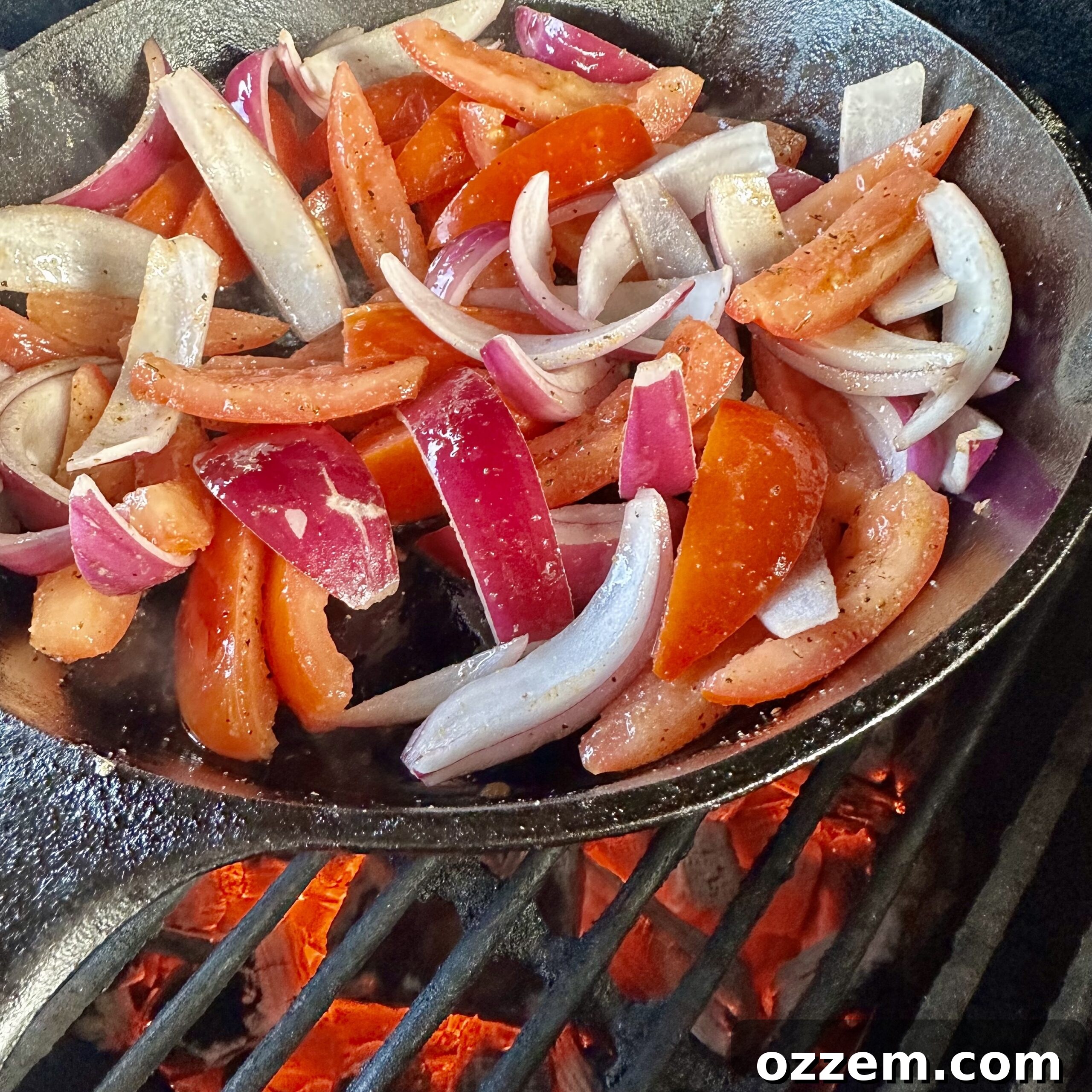 Colorful red onions and Roma tomatoes sautéing in a cast iron skillet over direct grill heat.