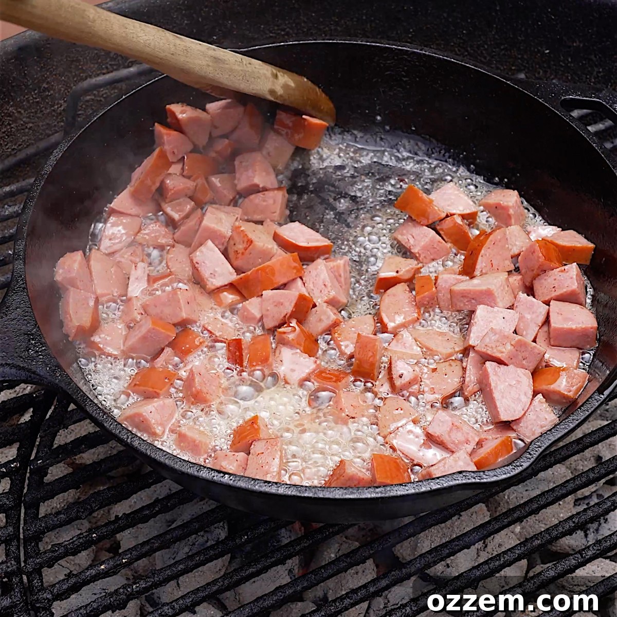 Diced Polish sausage beginning to brown in a cast iron skillet on the grill, surrounded by bacon grease.