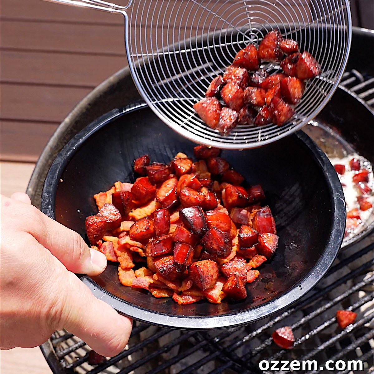 Cooked, golden-brown sausage pieces being transferred from a cast iron skillet into a bowl, joining the crispy bacon.