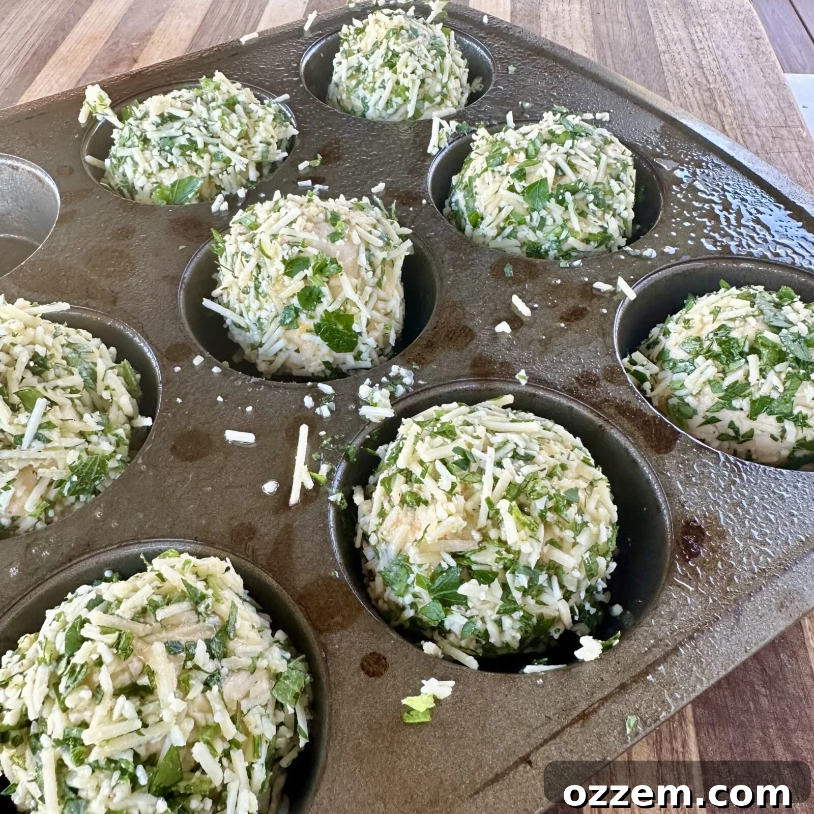 Savory Cheese Muffins 6 Biscuit balls generously coated with seasoned butter and shredded cheese, placed in a muffin pan, ready for baking.