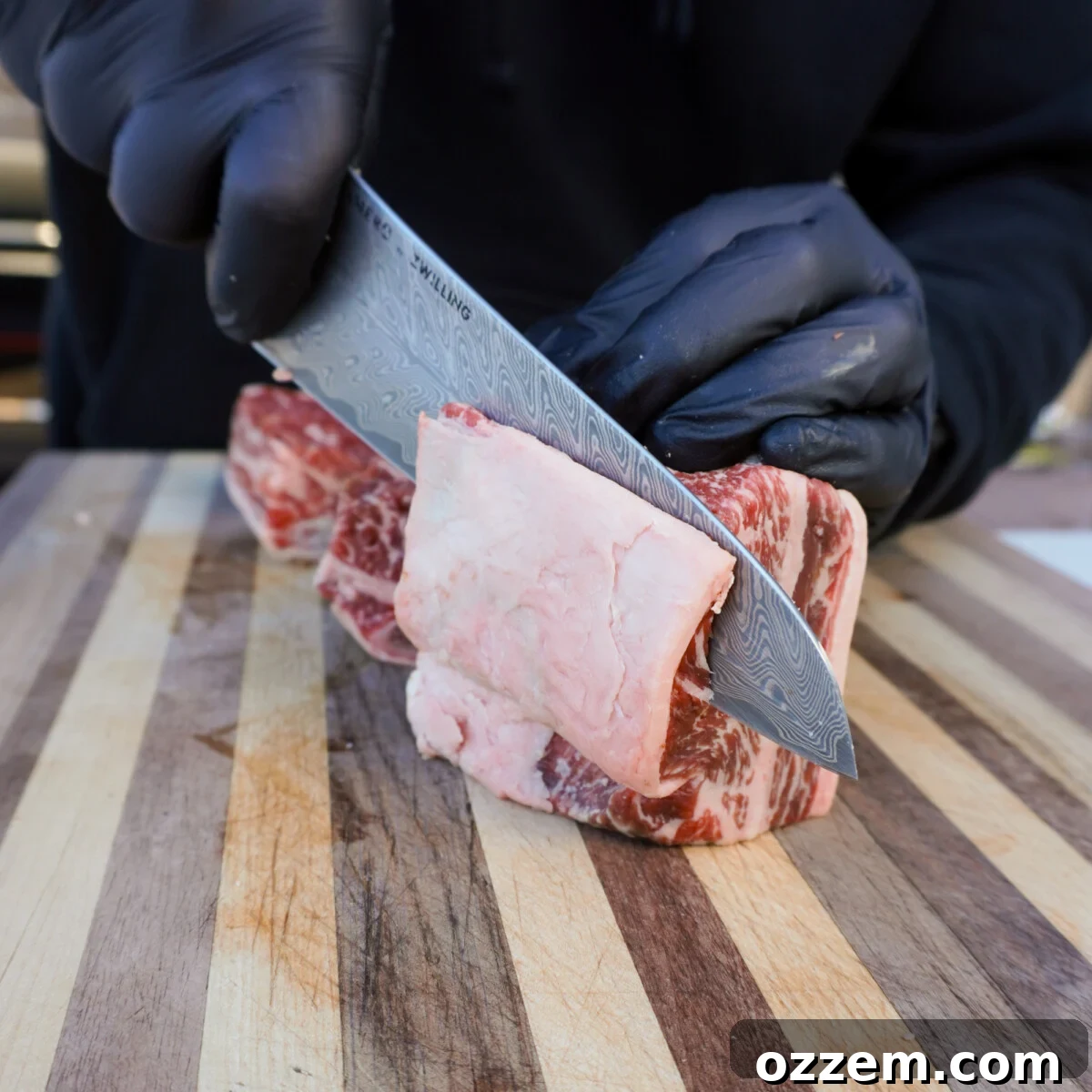 Velvet Smoke Ribs 4 A hand carefully removing the silver skin from a beef short rib, exposing the lean meat underneath.