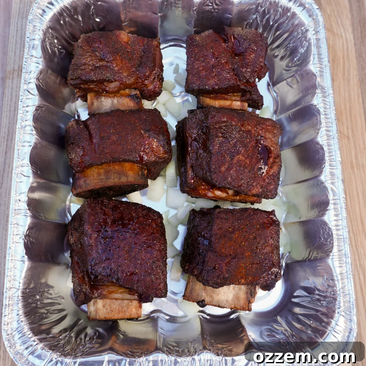 Velvet Smoke Ribs 9 Smoked beef short ribs carefully placed in a foil pan on a bed of diced onions, ready for the braising liquid.